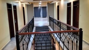 Una escalera con barandilla de metal y pasamanos de madera, que lleva a un rellano con vistas a un pasillo.