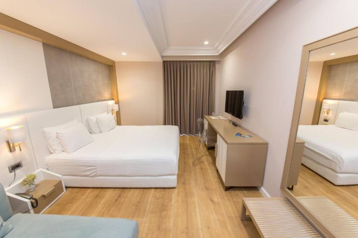Una habitación de hotel con una cama grande, un escritorio, un espejo y un televisor.