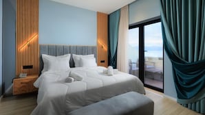A modern hotel room with a large bed, a wooden nightstand, a bench, and a view of the outdoors through a sliding glass door. - Hotel Brilant (Sarandë)