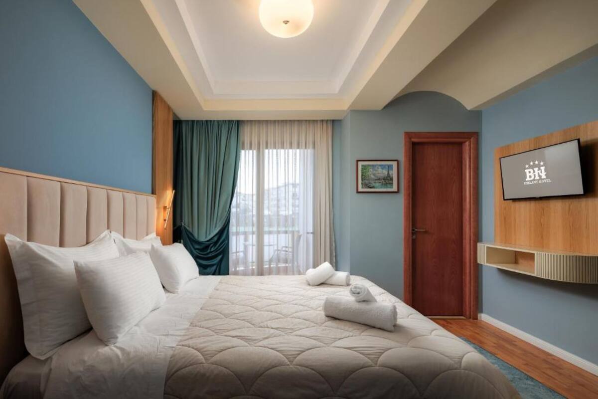 Habitación de hotel con cama, televisor montado en la pared, puerta y ventana con cortinas.