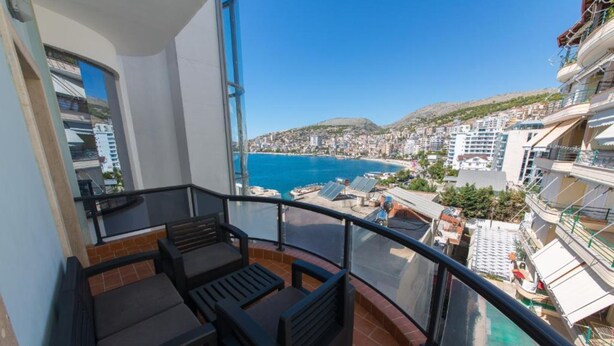 A balcony with outdoor furniture, a clear view of a coastal town, and a hillside in the background. - Hotel Brilant (Sarandë)