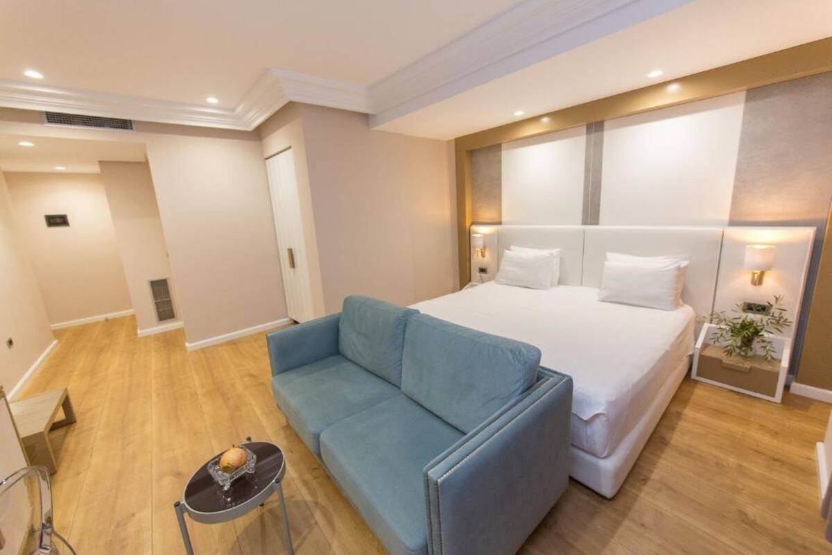 Una habitación de hotel moderna con una cama grande, un sofá azul y una mesita con un objeto decorativo.