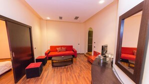 A modern living room with a red sofa, black ottomans, a glass coffee table, and a TV on a wooden cabinet. - Hotel Brilant (Sarandë)
