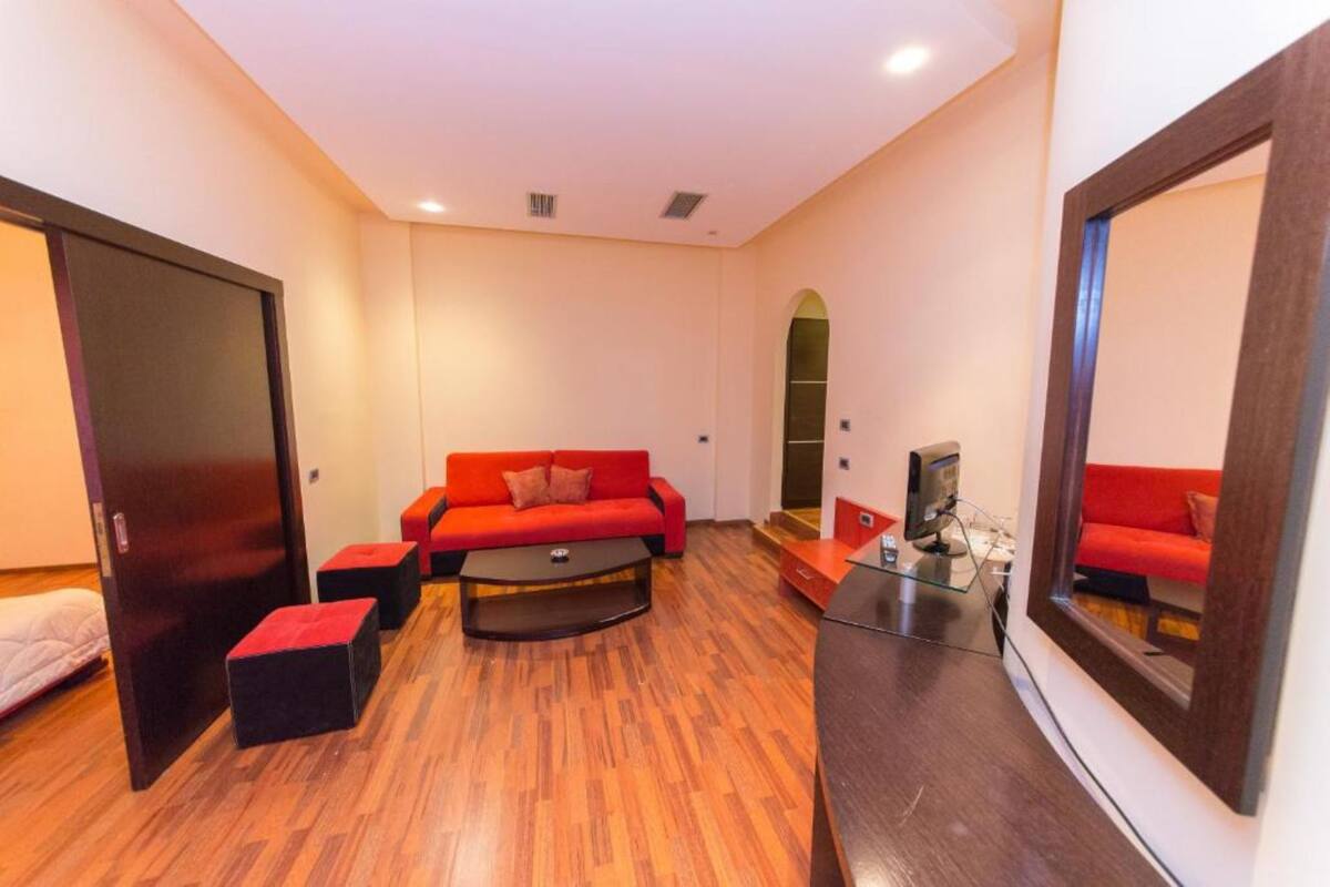 Una sala de estar moderna con un sofá rojo, otomanas negras, una mesa de centro de vidrio y un televisor sobre un mueble de madera.