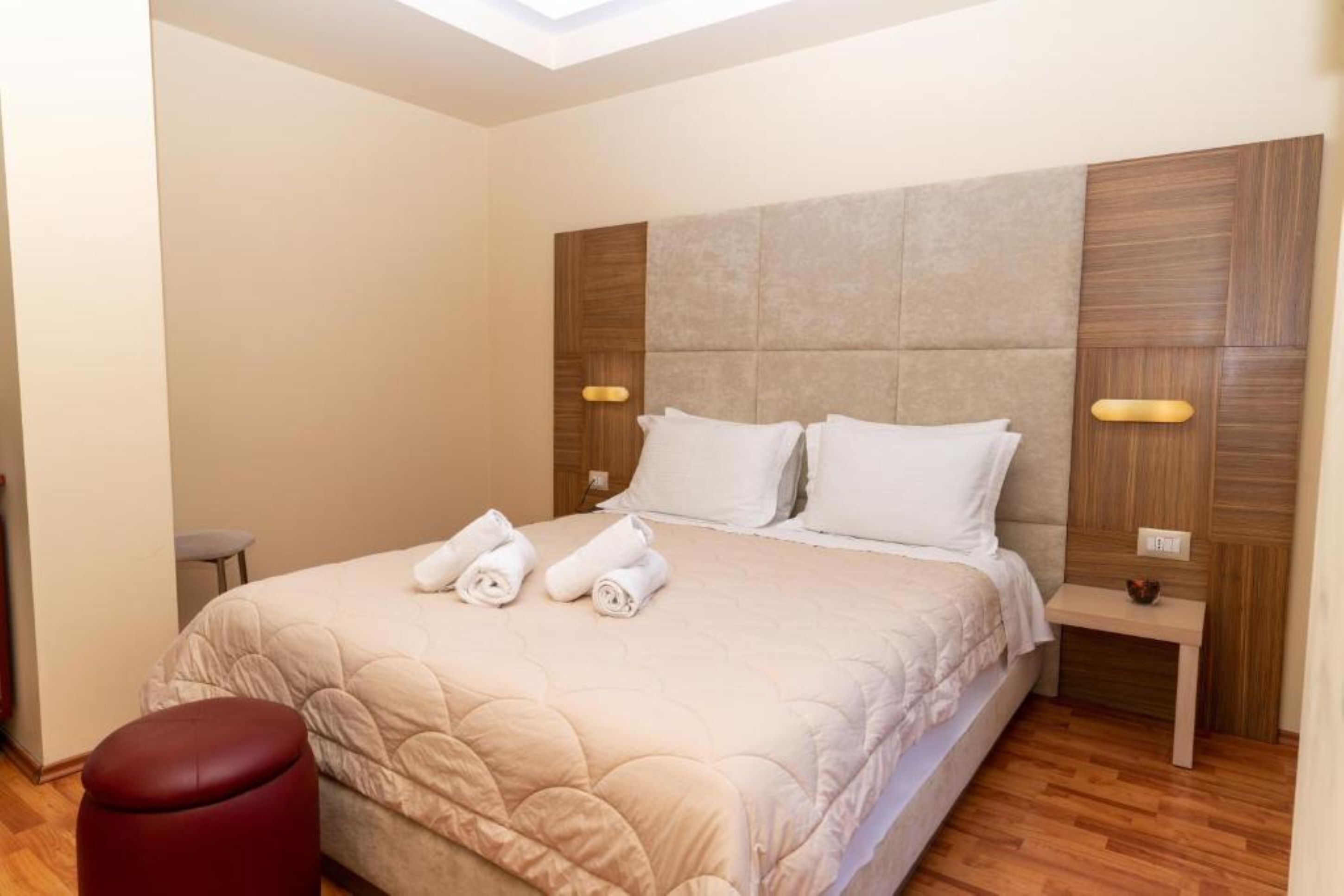 Ein Hotelzimmer mit einem großen Bett, zwei Nachttischen, einem roten Hocker und einem Oberlicht.