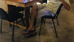 A person sitting at a wooden table with a laptop, a cup, and a bottle.