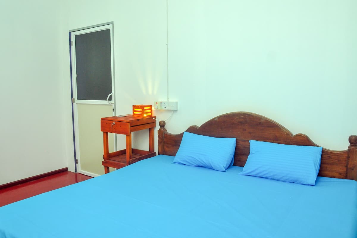 A room with a bed, a nightstand, a window, and a wall socket.