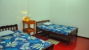 A room with two single beds, each with a floral-patterned bedspread, a bedside table with a lamp, and a red floor.