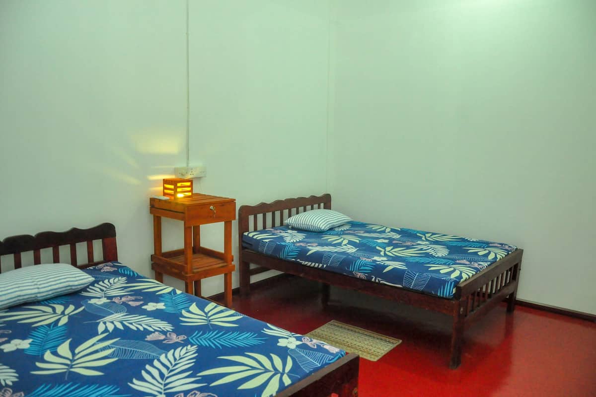 A room with two single beds, each with a floral-patterned bedspread, a bedside table with a lamp, and a red floor.