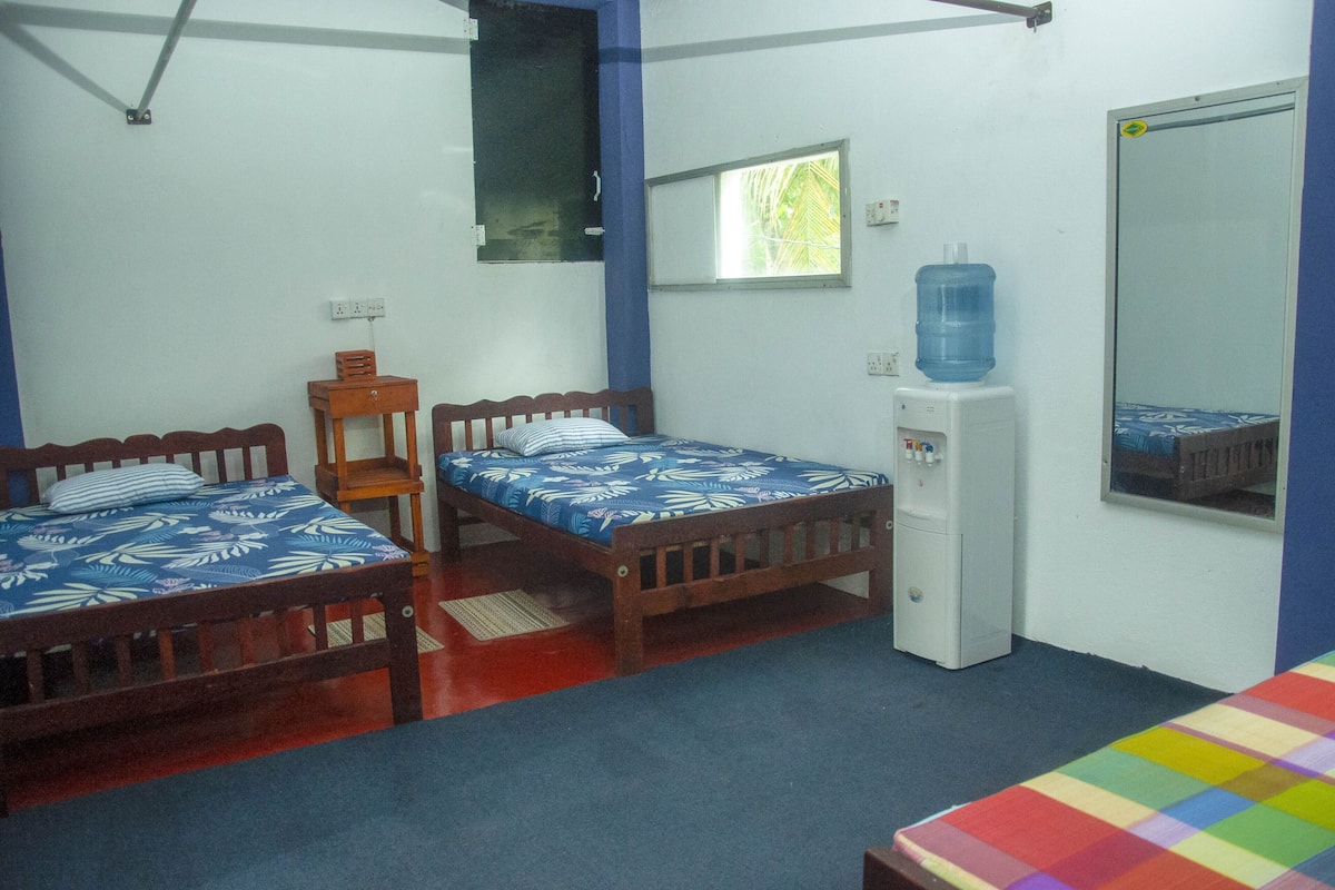 A small, clean room with two wooden beds, a small table, a water dispenser, and a mirror.