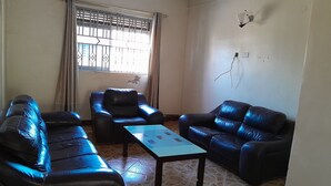 A living room with a sofa set, a coffee table, and a window with curtains. - Blue Star Apartments (Entebbe)