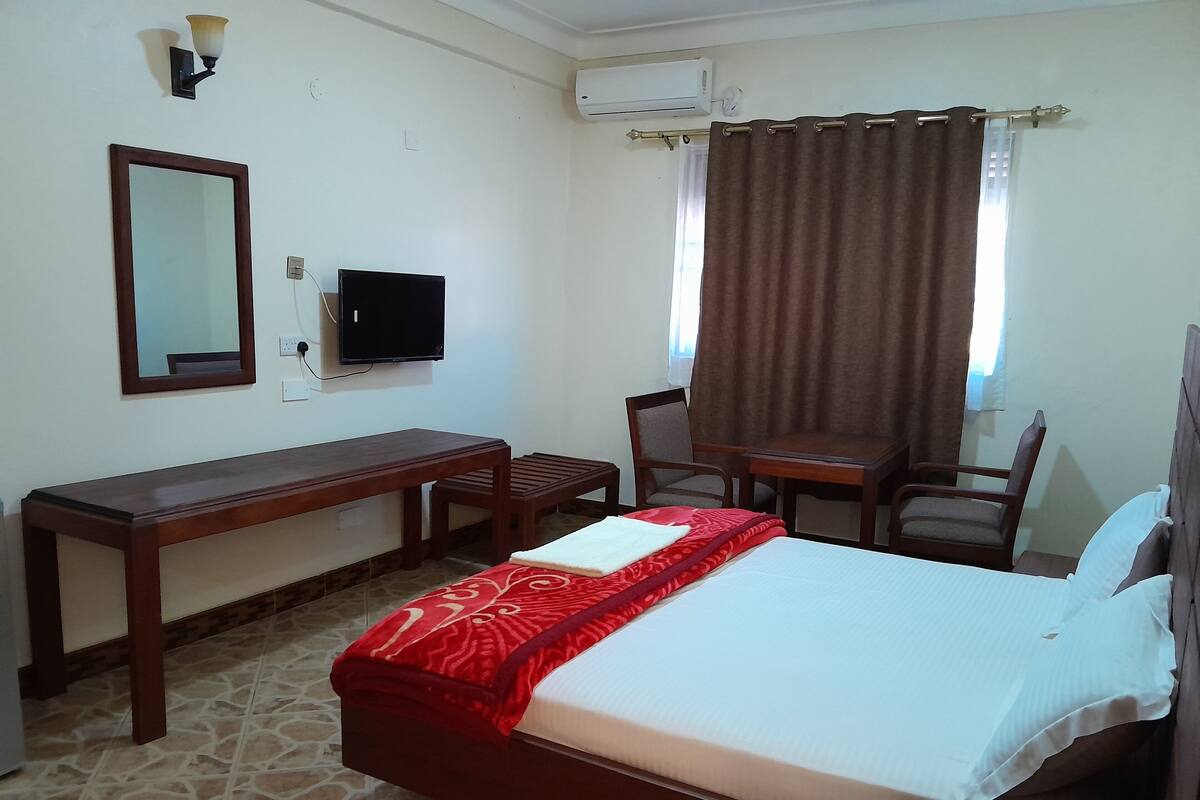 A hotel room with a bed, a desk, a chair, a TV, and a window with curtains.