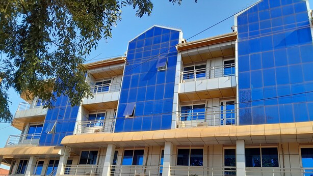 A multi-story building with a blue facade, multiple balconies, and a ground-level entrance with a sign for a bank. - Blue Star Apartments (Entebbe)