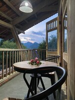 Um deck de madeira com mesa e cadeiras, com vista para uma paisagem montanhosa.