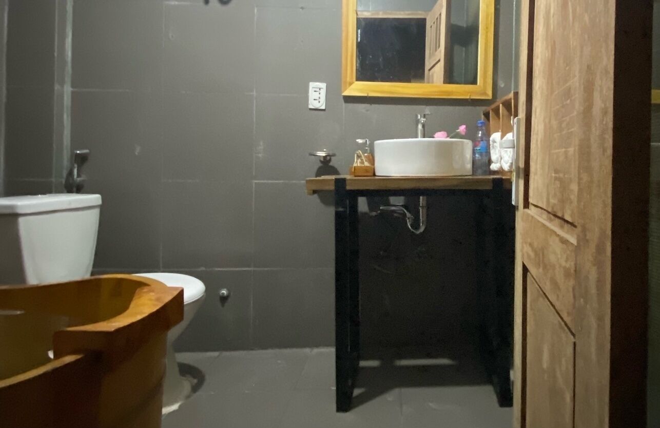 A bathroom with a wooden bathtub, a white sink, and a mirror above it.