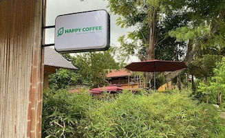 Placa de Happy Coffee com fundo de bambu e área externa com mesas e guarda-sóis vermelhos.