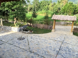 Um pátio de pedra com um pequeno jardim, cerca de madeira e uma estrutura de pérgola.