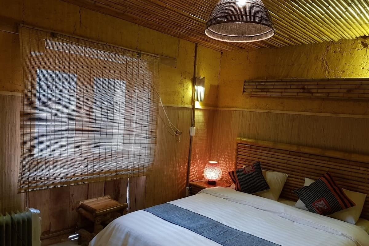 Une pièce en bois avec un lit, une table de chevet, une lampe et une fenêtre avec des stores.
