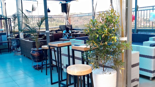 An outdoor patio area with tables and chairs, a potted plant, and a view of the cityscape. - JB suites and lounge (Kampala)