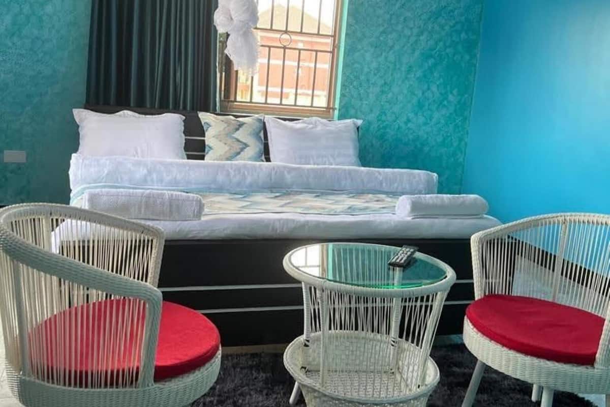 Une chambre à coucher avec un lit, deux fauteuils en osier blanc dotés de coussins rouges, une petite table ronde et un ventilateur de plafond.