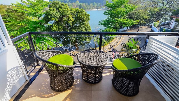 A balcony with wicker furniture and a view of a lake and forest. - Devon Rest (Kandy)