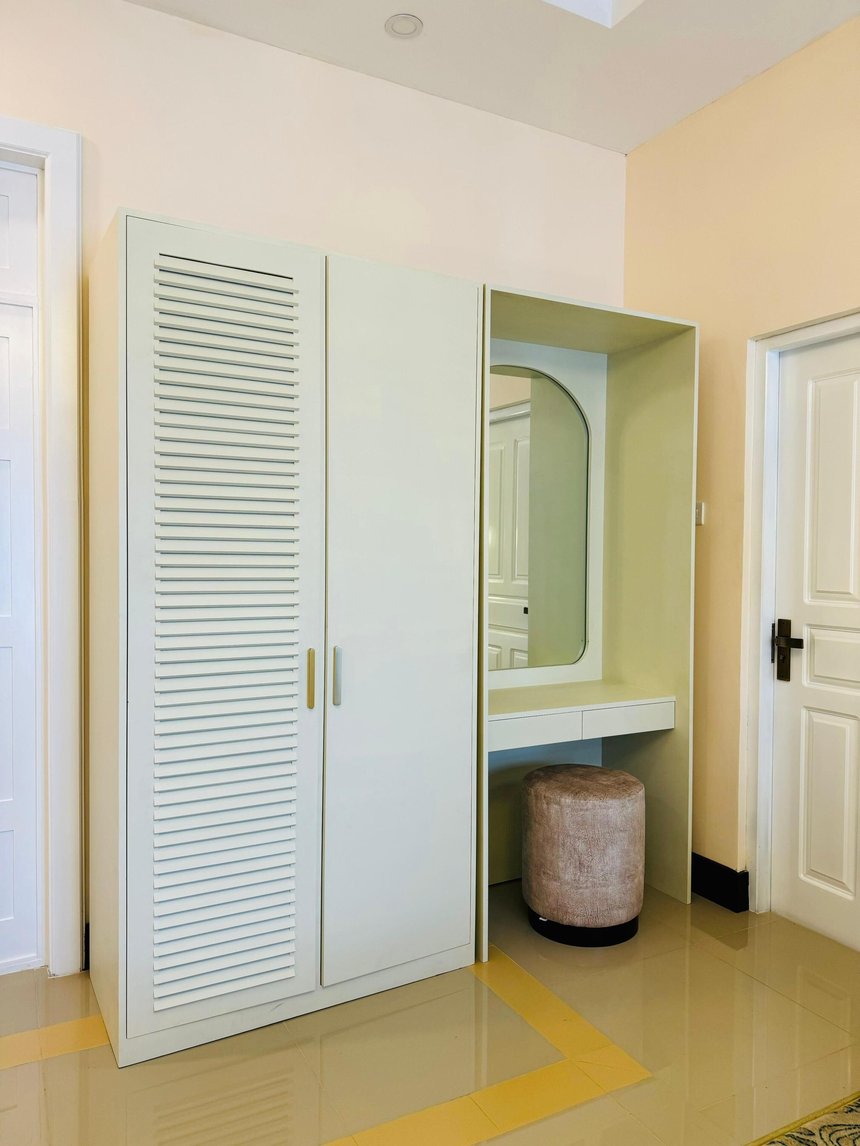 A room with a white wardrobe, a mirror, and a small trash bin.