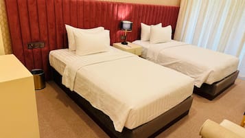Habitación de hotel con dos camas, un cabecero rojo, una mesita de noche con una lámpara y un bote de basura.