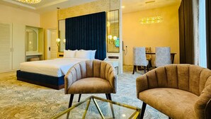 A hotel room with a bed, two armchairs, a glass coffee table, a mirror, and a chandelier. - Devon Rest (Kandy)