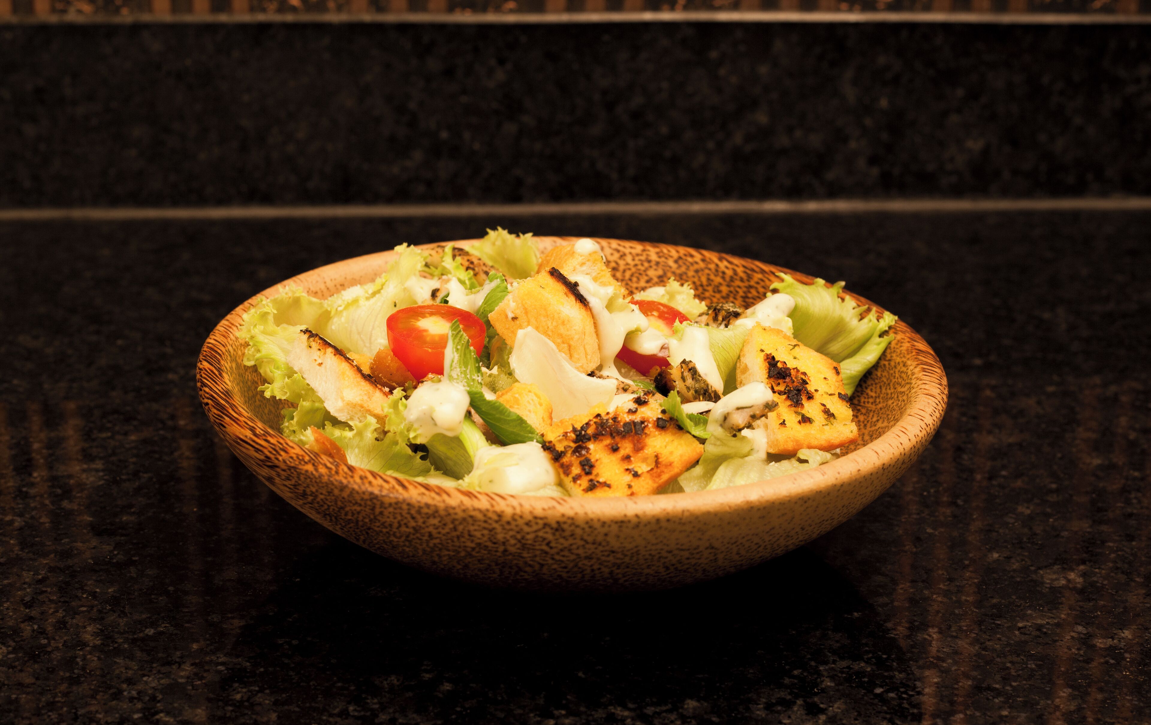 A bowl of salad with grilled chicken, lettuce, and tomatoes on a dark countertop.