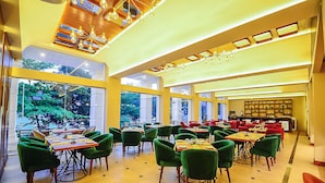 A spacious restaurant with green upholstered chairs and tables, large windows offering a view of greenery, and a ceiling with hanging spherical lights. - Devon Rest (Kandy)