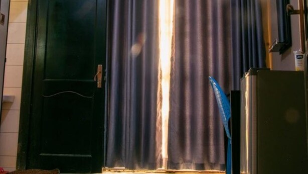 Una habitación con una puerta de color oscuro, una ventana con cortinas oscuras y un equipo de aire acondicionado fijado a la pared.