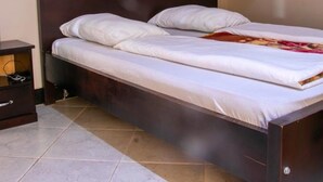 Una cama individual con cabecera oscura en una habitación con suelo de baldosas.