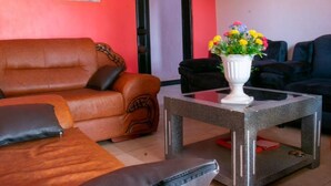 Una sala de estar con un sofá de cuero marrón, un sillón negro y un jarrón blanco con flores sobre una mesa de vidrio.