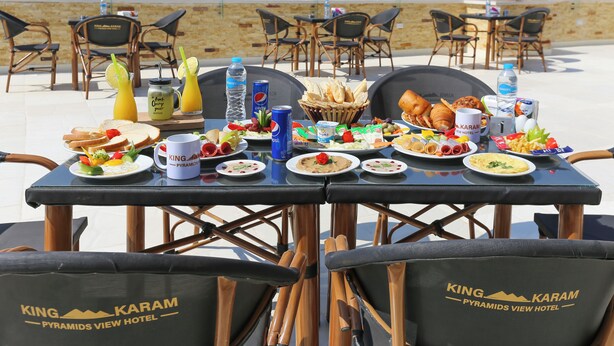 A breakfast table with various foods and drinks, set against a view of the pyramids. - Venus Pyramids Inn (Giza)