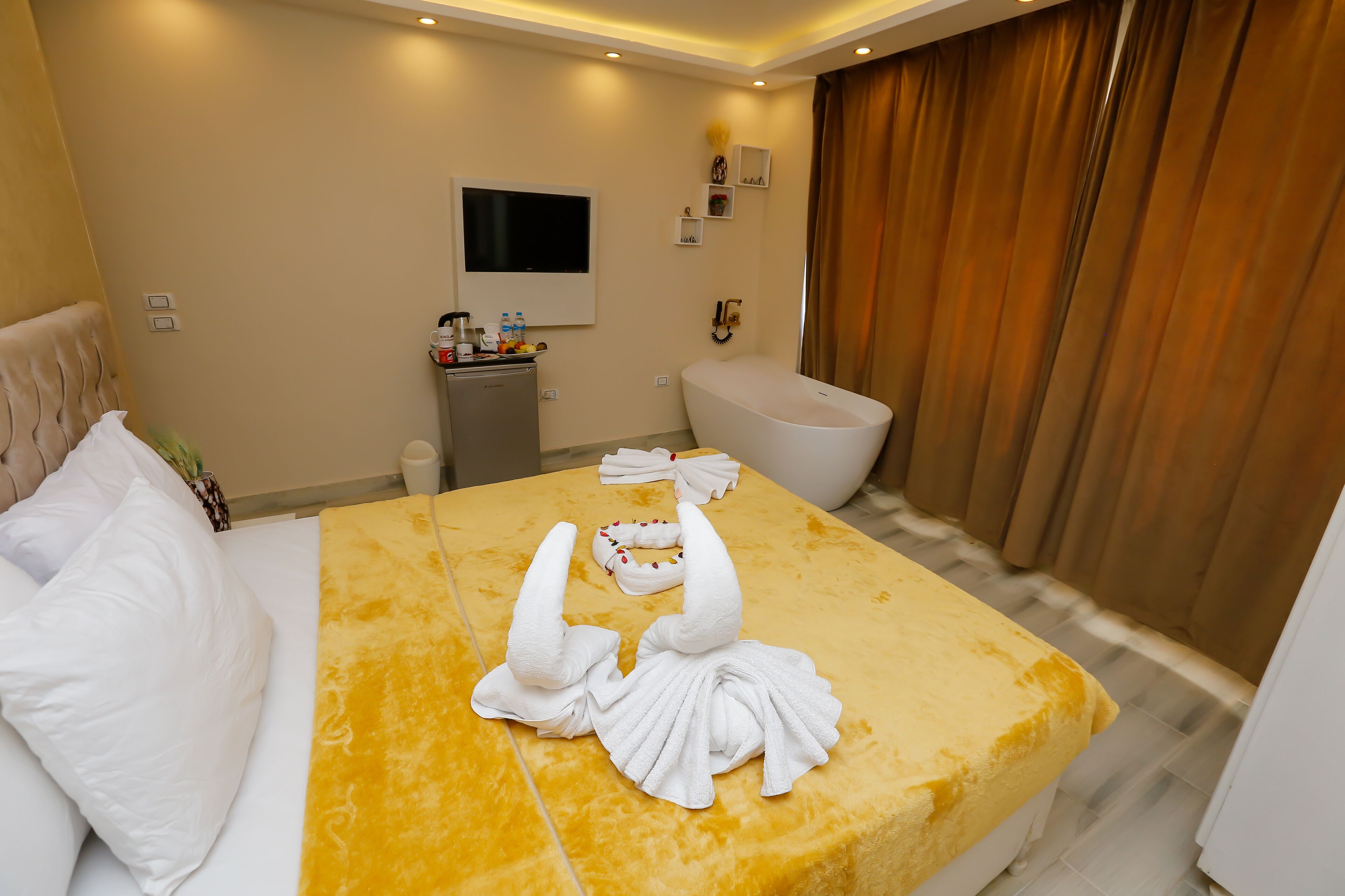 A hotel room with a bed, a television, a minibar, a toilet, and a shower area.