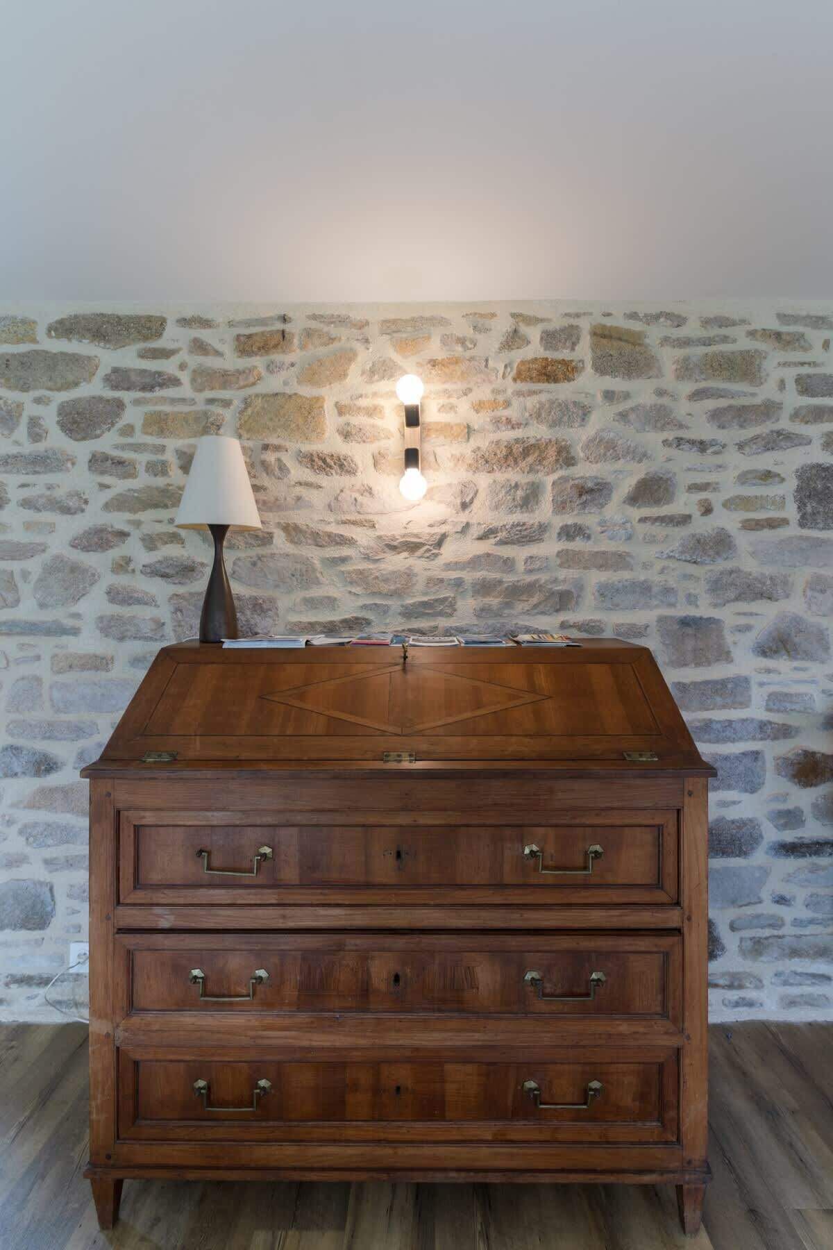 Een houten dressoir tegen een stenen muur, met een wandlamp.