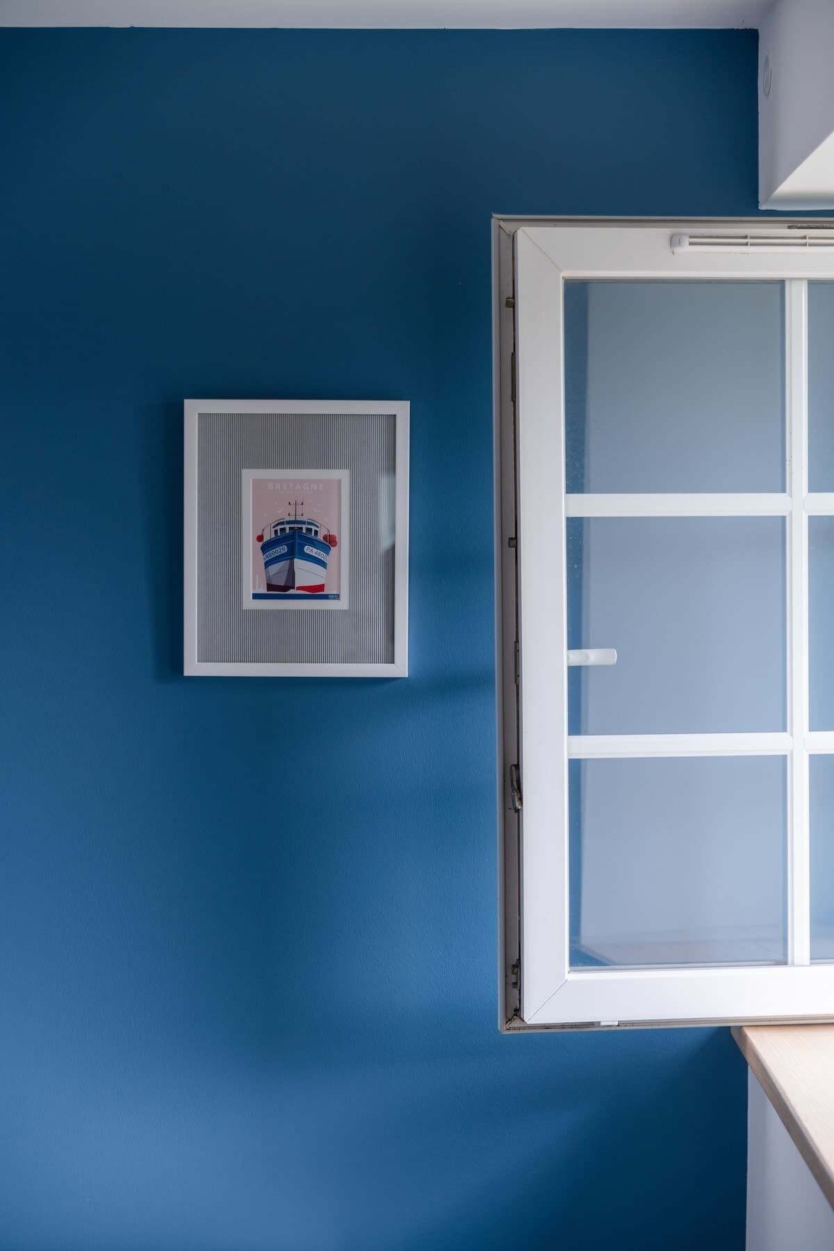 Une pièce avec un mur bleu, un tableau encadré et une fenêtre à cadre blanc.