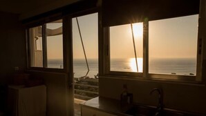 A kitchen with a view of the ocean at sunset, a sink, and a table with chairs.