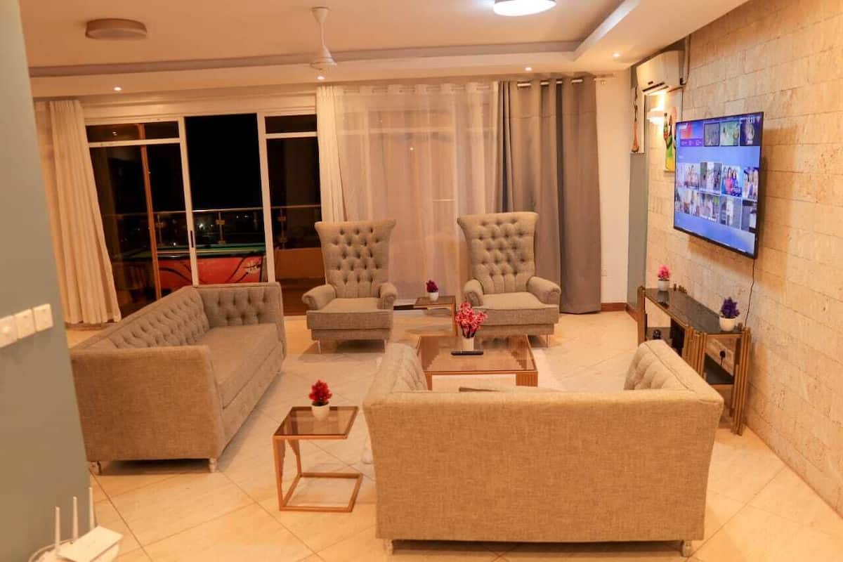 Ein modernes Wohnzimmer mit einer Couch, zwei Sesseln, einem Couchtisch und einem an der Wand montierten Fernseher.