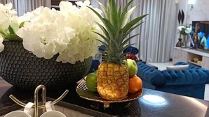 A modern kitchen with a black countertop, white flowers, a pineapple, and a bowl of fruit.