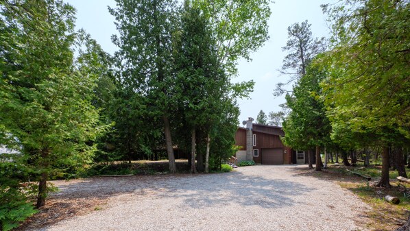 A gravel driveway leading to a modern house surrounded by dense trees.