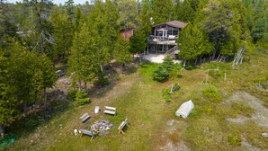 An aerial view of a cabin surrounded by dense forest, with a deck and outdoor seating area.