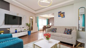 A modern living room with a sofa, blue armchairs, a coffee table, and a TV.