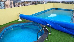 Two swimming pools with blue tiles, surrounded by artificial grass, and a yellow wall in the background.