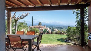 Une terrasse extérieure avec une table et des chaises, donnant sur un jardin et un paysage lointain.