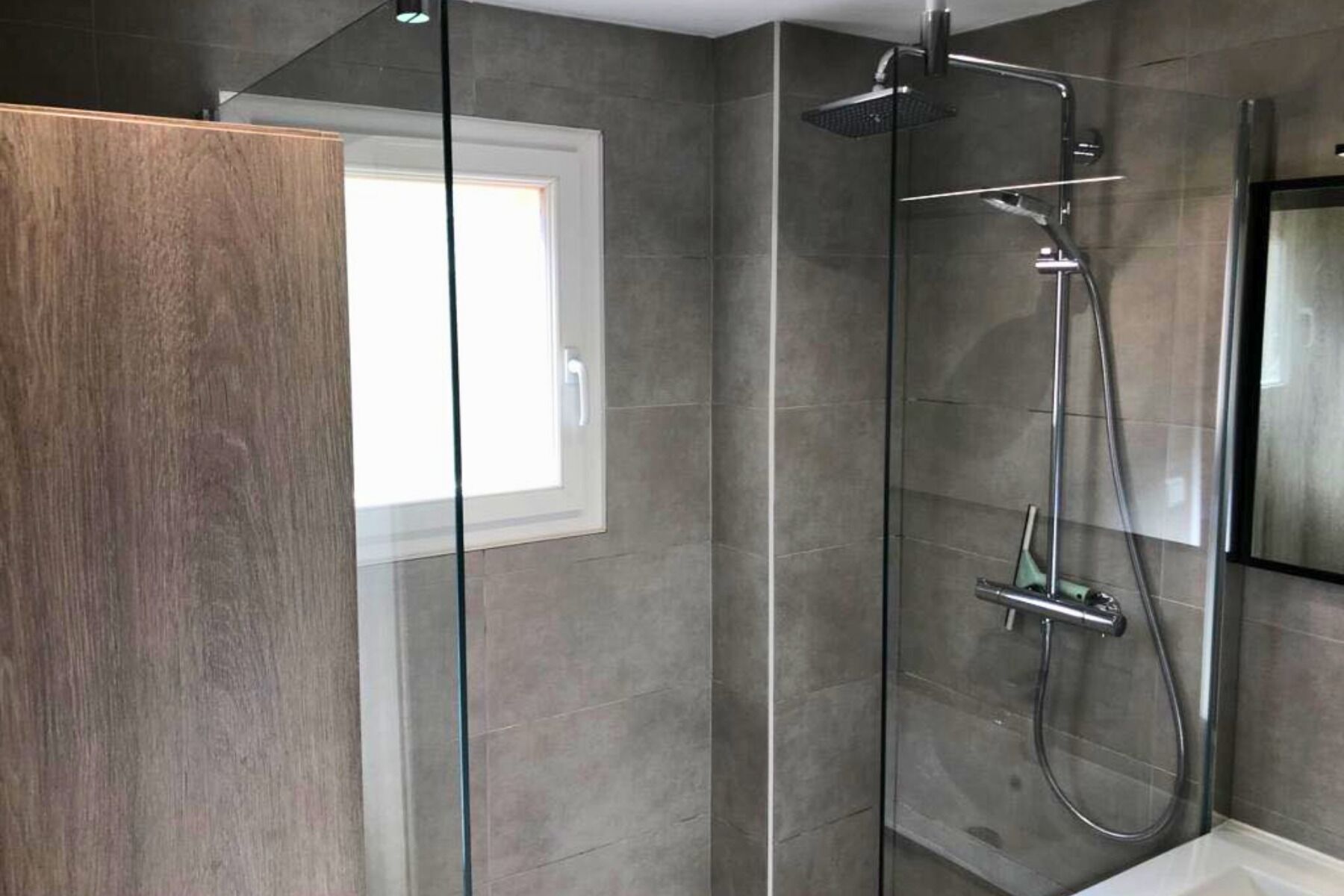 Una ducha moderna con cabina de vidrio, cabezal de ducha manual y grifo monomando.