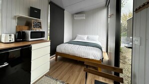 A compact bedroom with a bed, a kitchenette with a microwave, toaster, and kettle, and a view through a window.