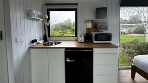 A compact kitchen with a sink, a microwave, and a toaster. There's a window with a view of a garden and a parked car outside.