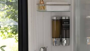 A bathroom with a white sink, a glass shelf with a bottle and a towel, and a hand sanitizer dispenser.