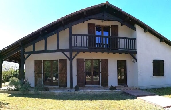 A two-story building with a balcony, large windows, and a covered porch area.